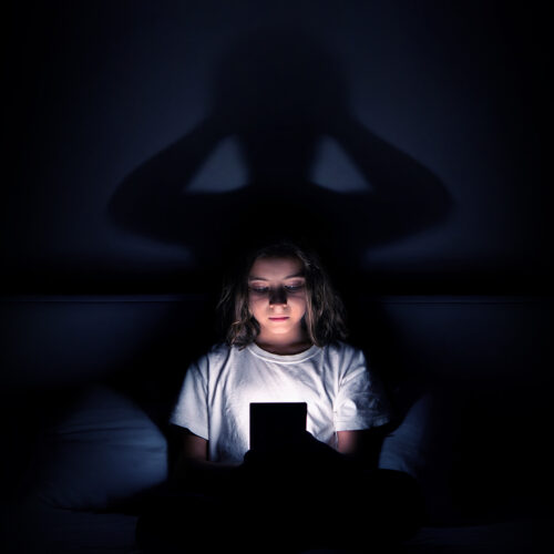 Minore al buio con smartphone e ombra inquietante: simbolo della dipendenza da social.