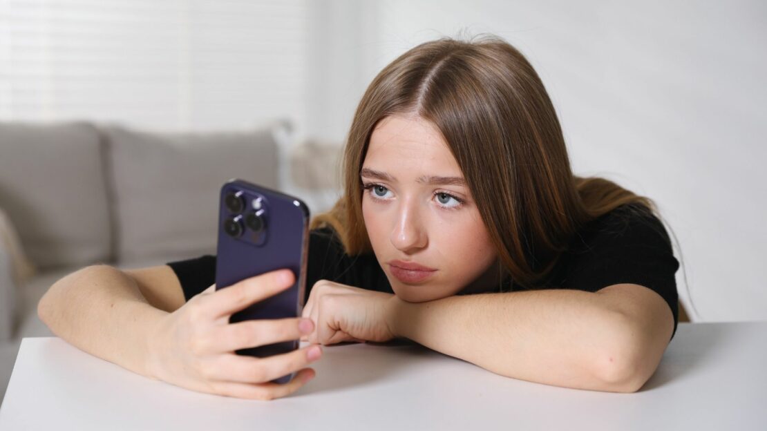 Ragazza adolescente che guarda lo smartphone con espressione assente, simbolo del fenomeno del doomscrolling e della dipendenza da social.