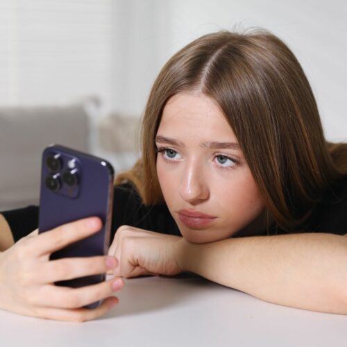 Ragazza adolescente che guarda lo smartphone con espressione assente, simbolo del fenomeno del doomscrolling e della dipendenza da social.