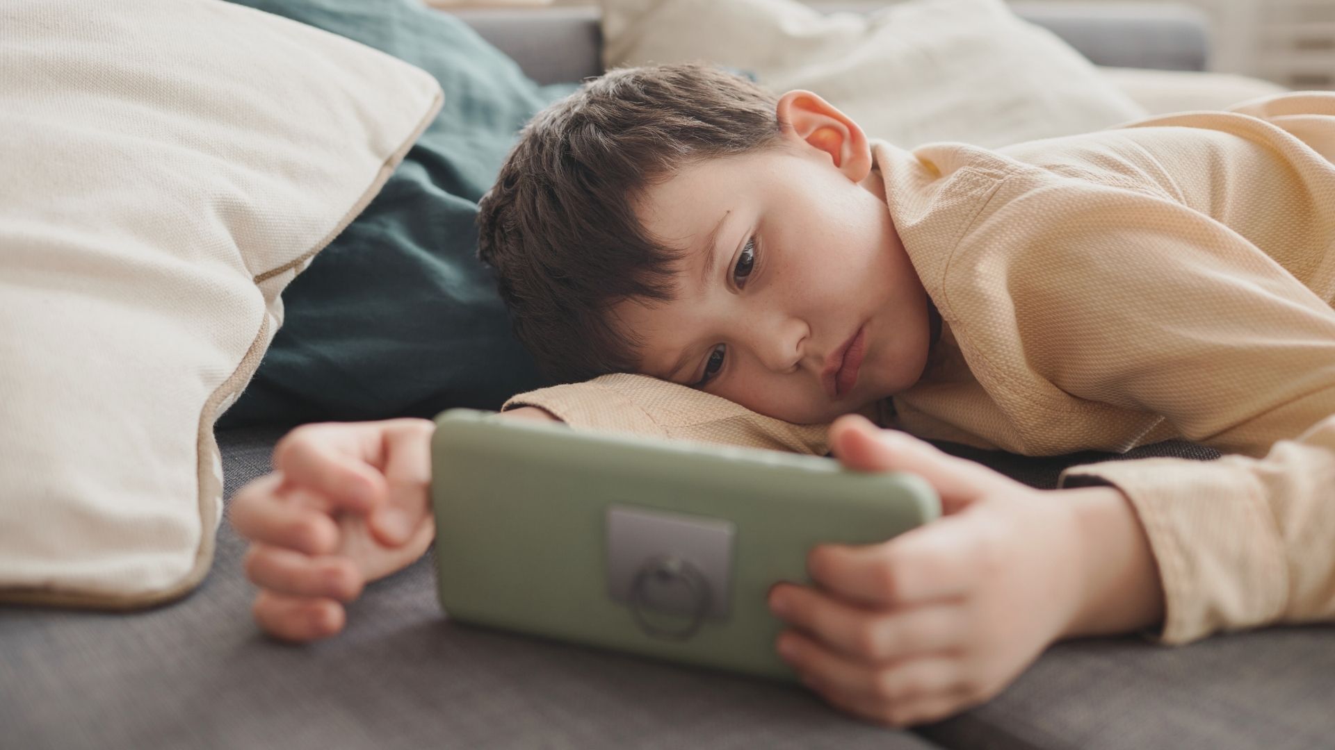 Bambino completamente assorto e apatico davanti allo schermo di uno smartphone, a rischio di ricompense dopaminergiche artificiali e isolamento.